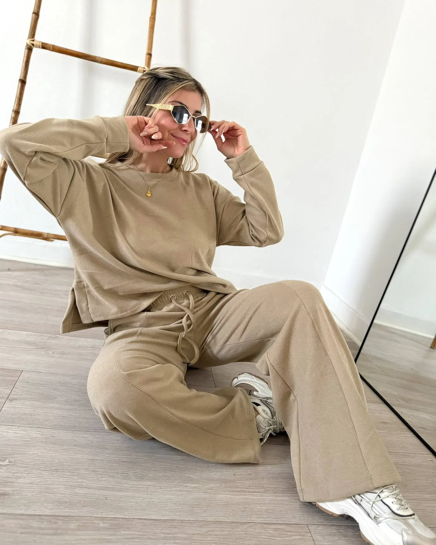 Conjunto de buzo y pantalón wide leg en tono camel, sobre pared blanca y piso de madera clara